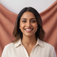 Joyful portrait of a smiling South Asian woman in her late 20s, looking at the camera, with a terracotta and dusty lilac back